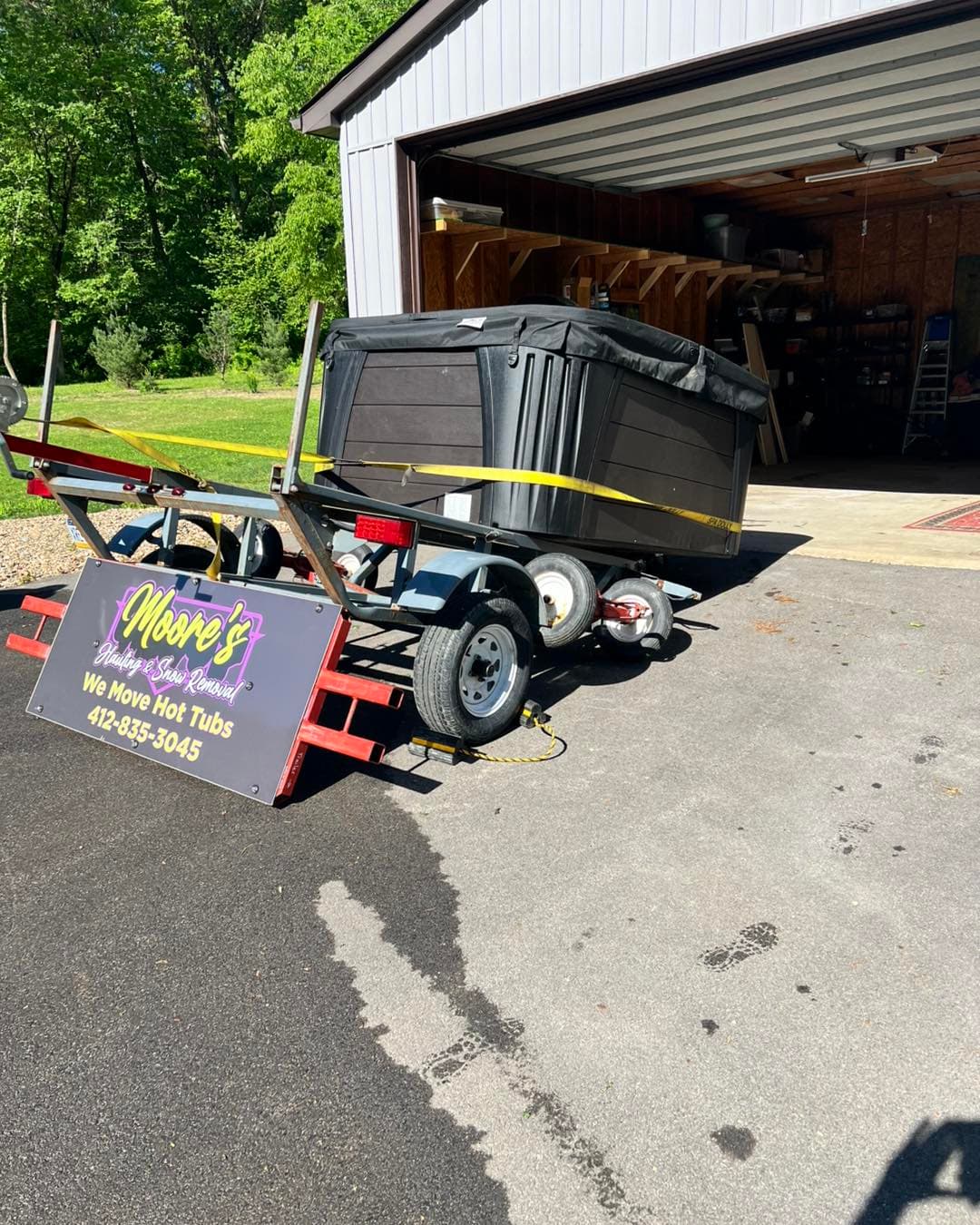 Hot tub strapped to a trailer next to a "We Move Hot Tubs" sign